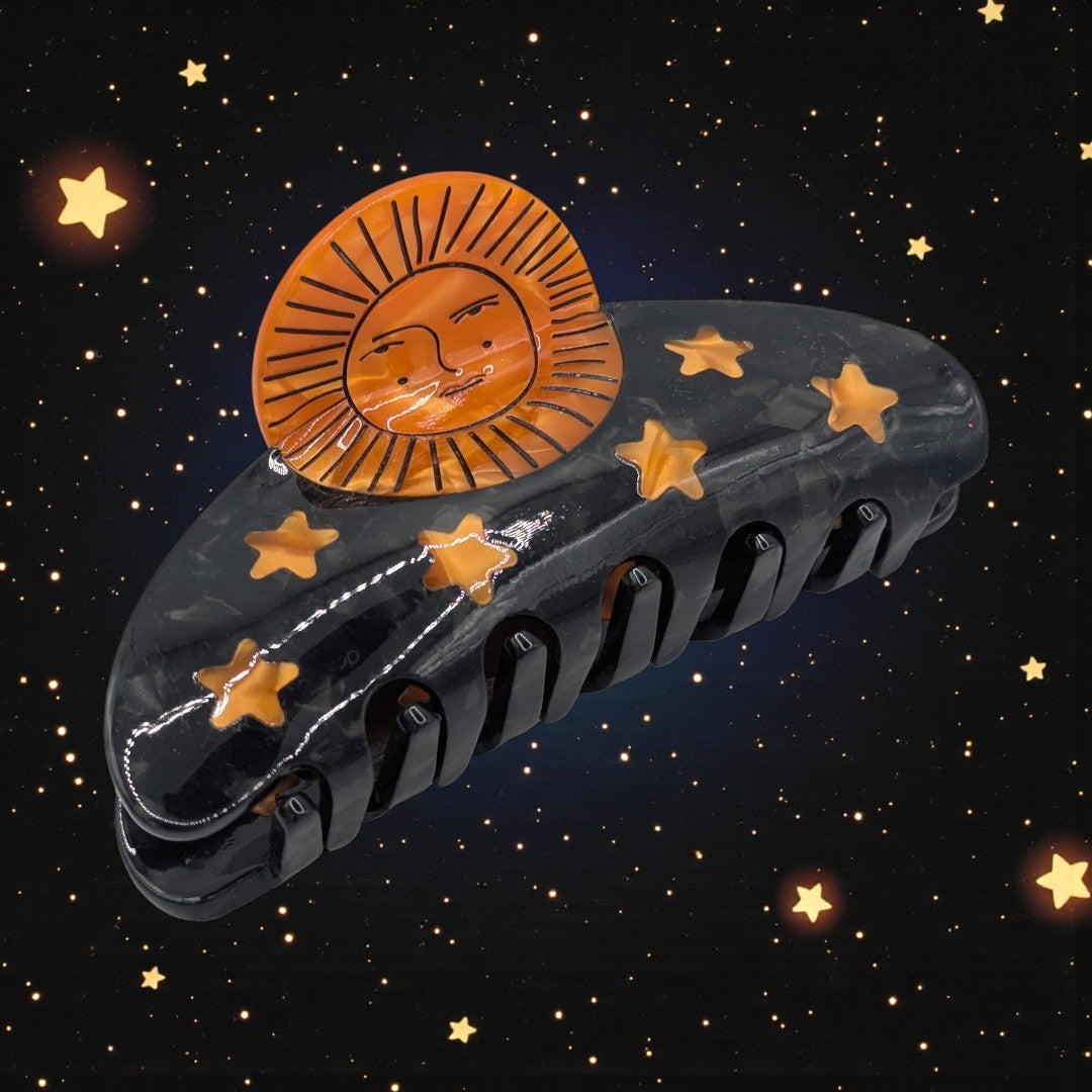 A black claw clip with orange sun and stars