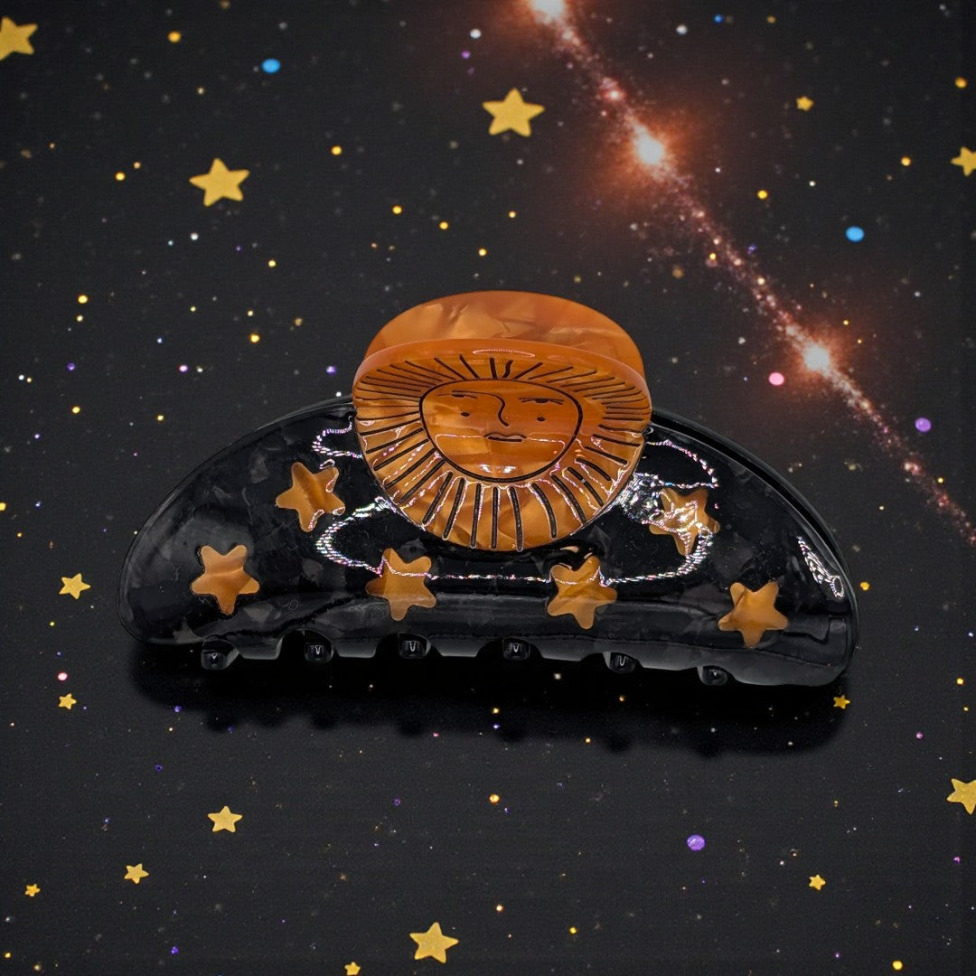 A black claw clip with orange sun and stars