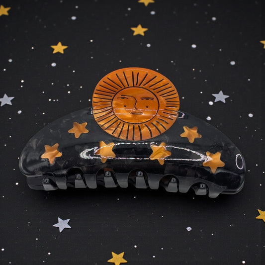 A black claw clip with orange sun and stars